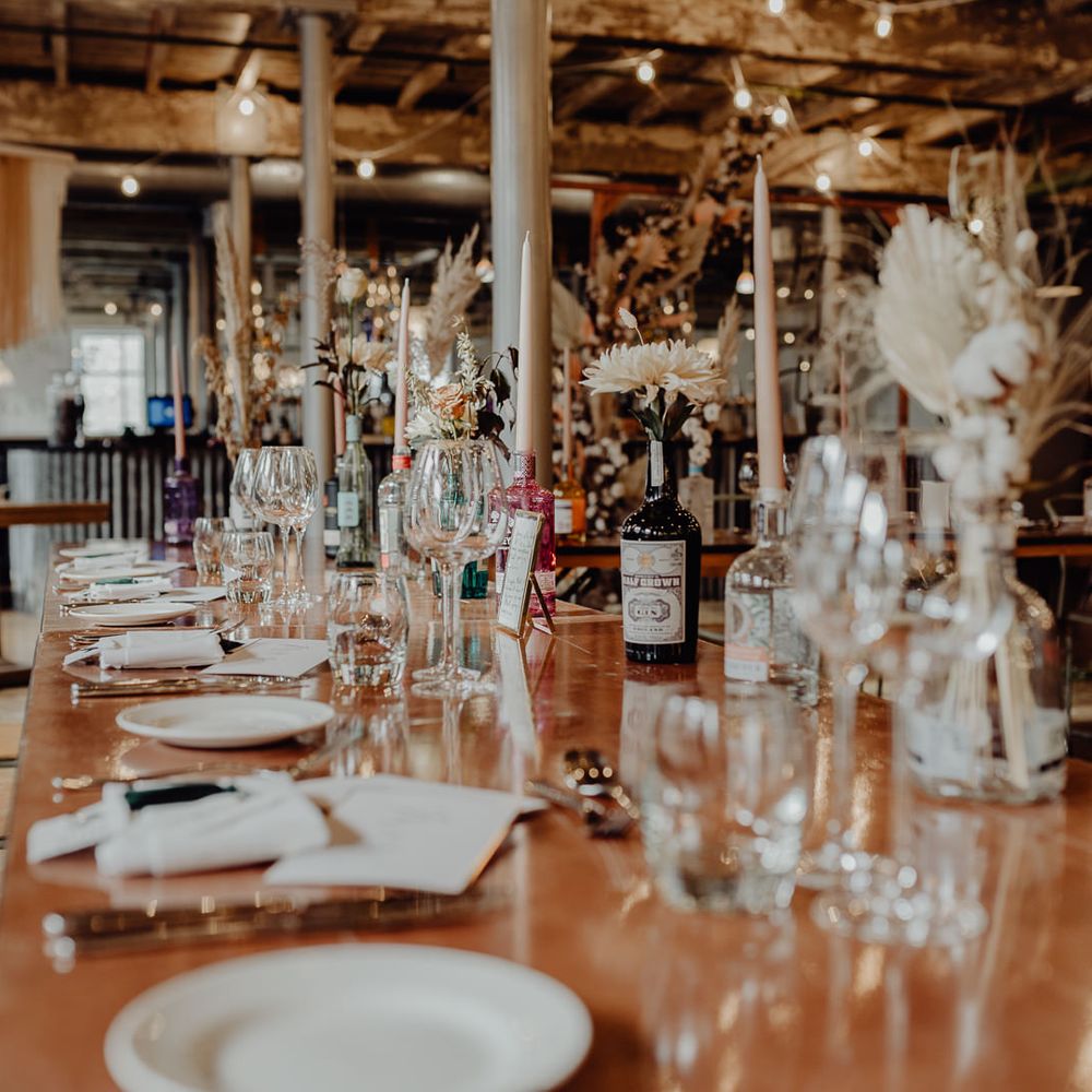 Bottles of gin filled with neutral taper candles and dried wedding flowers 