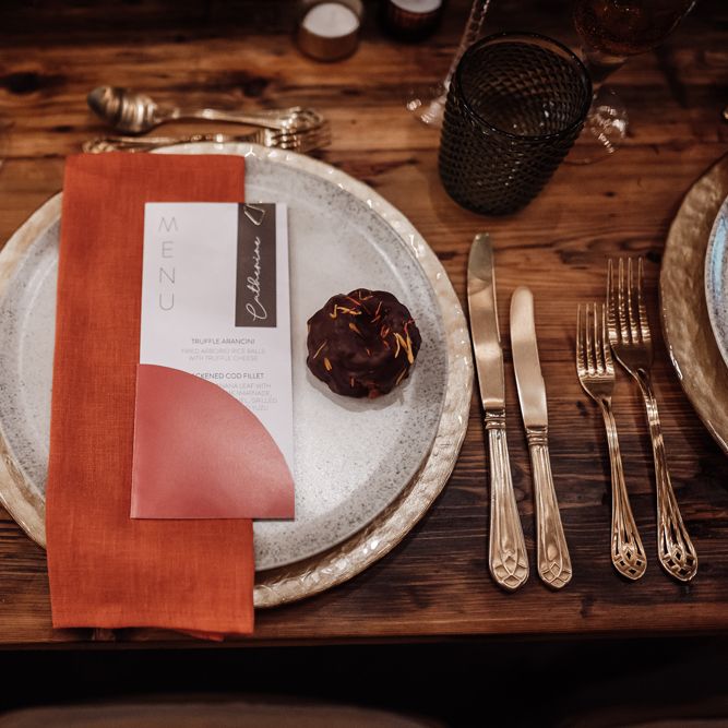Place setting with dappled tableware, orange napkin and contemporary menu sign 