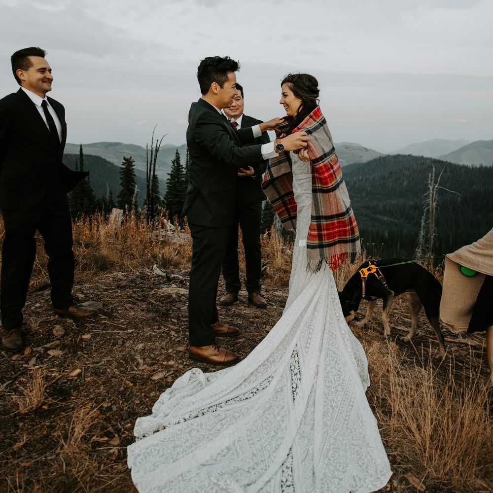 Groom covers bride with tartan blanket atop Montana moutains