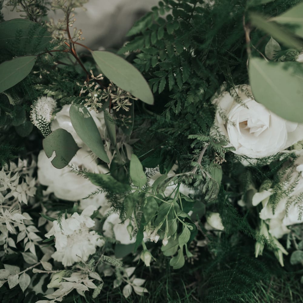 Close up if white and green wedding bouquet with white roses, olive leaves and green ferns.