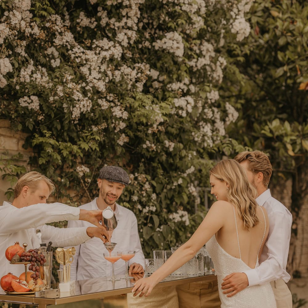 Bride in an embellished Made With Love dress standing at the outdoor mobile bar with her husband in a beige suit 
