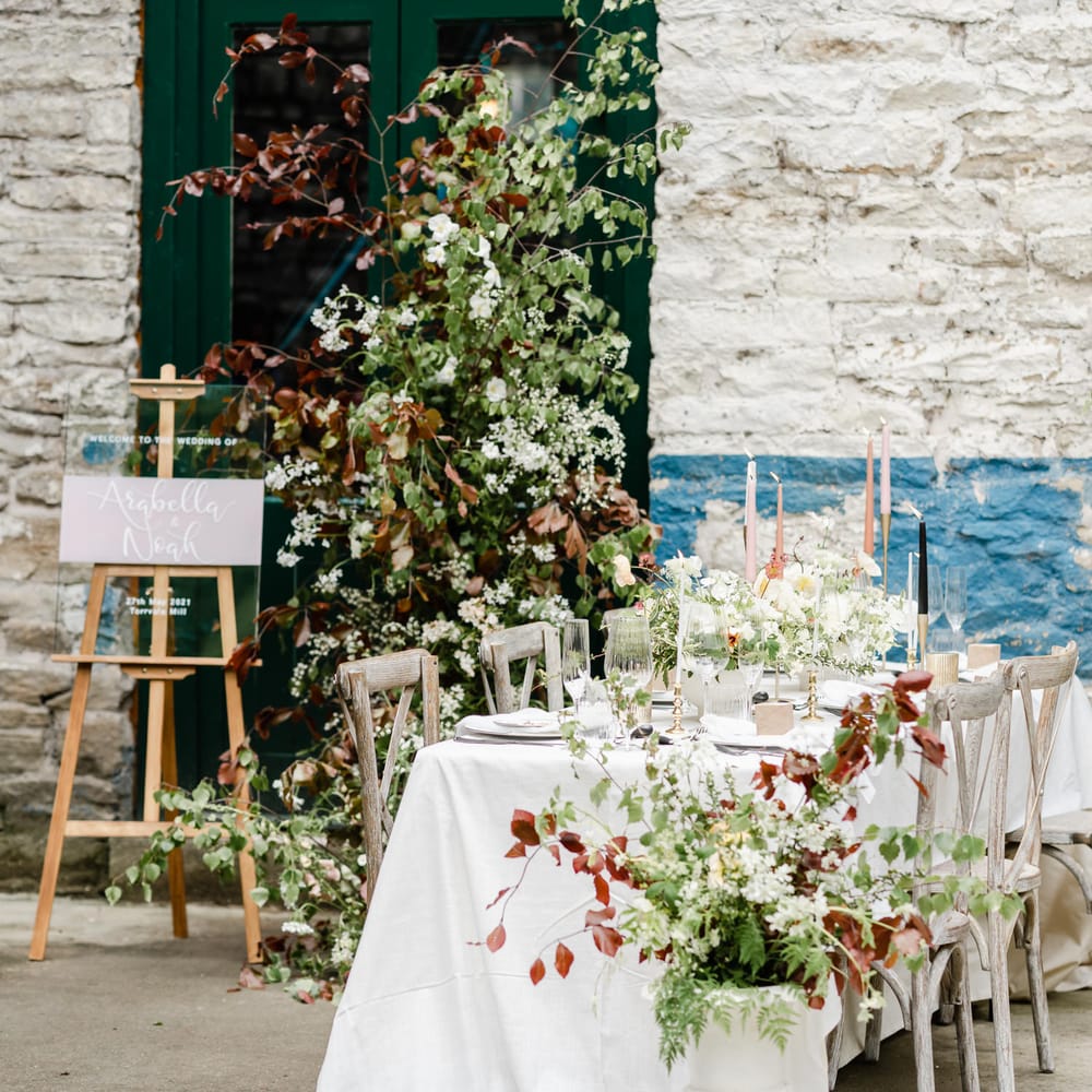Elegant wedding reception table decor at Torr Vale Mill with taper candles, floral arrangements and acrylic signs 