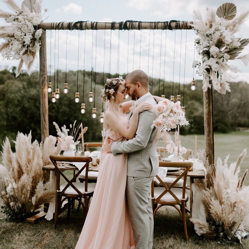 Outdoor boho reception at Waresley Park Estate with light installation and dried flowers and the bride in a blush pink loose fitting jumpsuit 