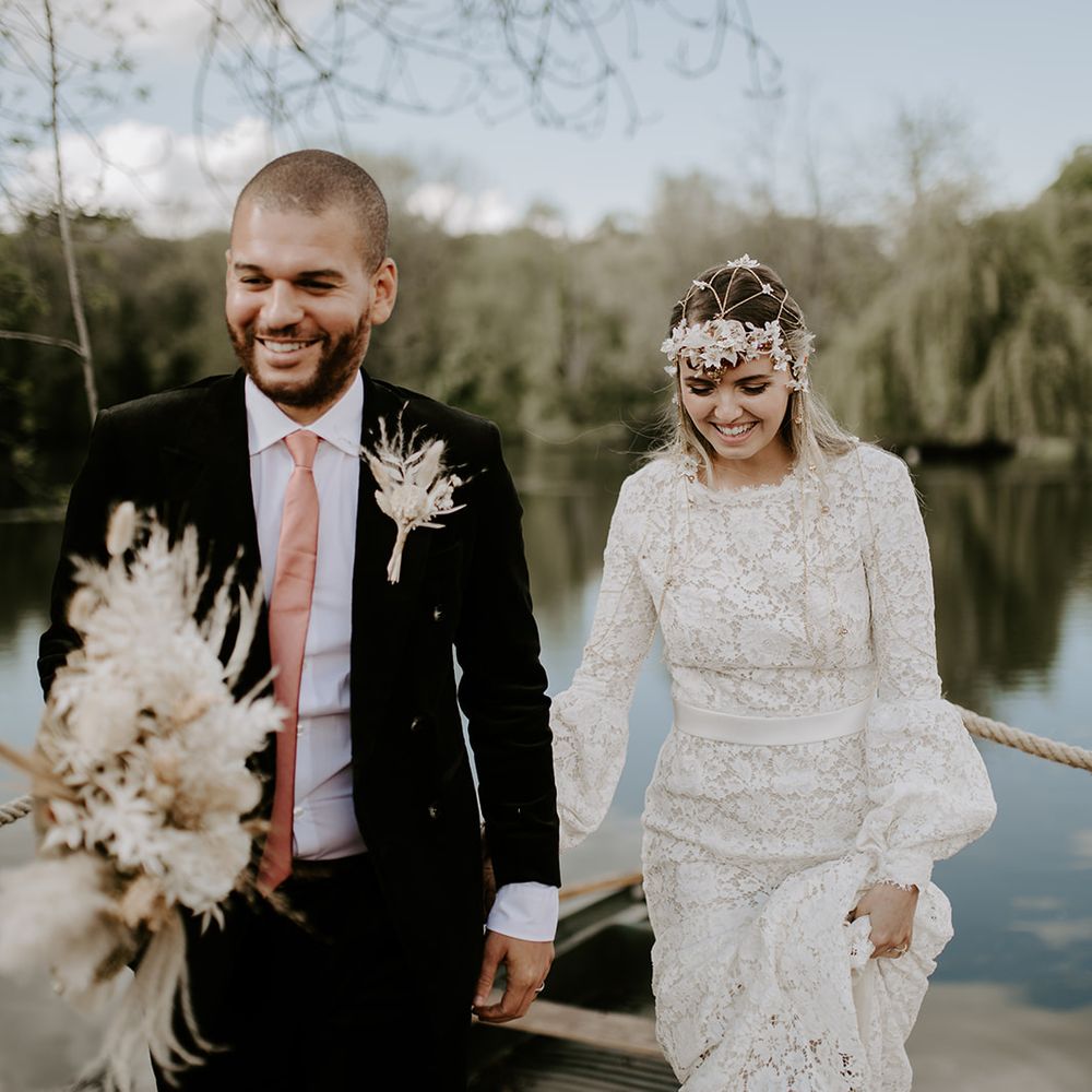 Groom in a black corduroy jacket wearing a pink tie holding hands with his bride in a lace wedding dress with long sleeves