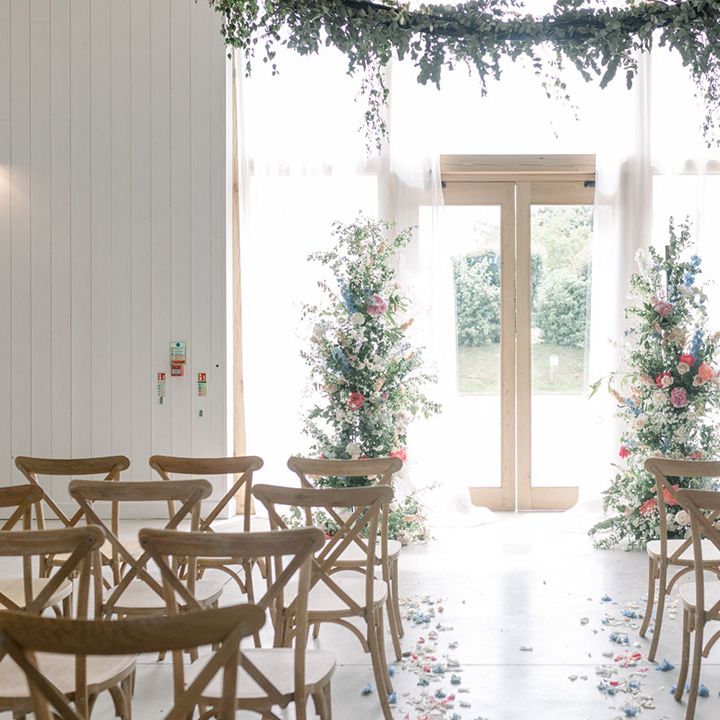The White Barn wedding venue ceremony room with petal lined aisle and vertical floral arrangements at the altar in front of the window 