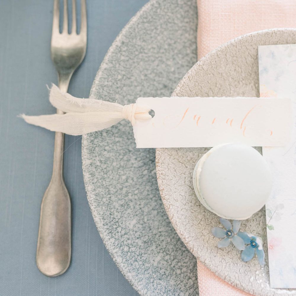 Elegant place setting with pattern tableware, name place card and macaroon wedding favour