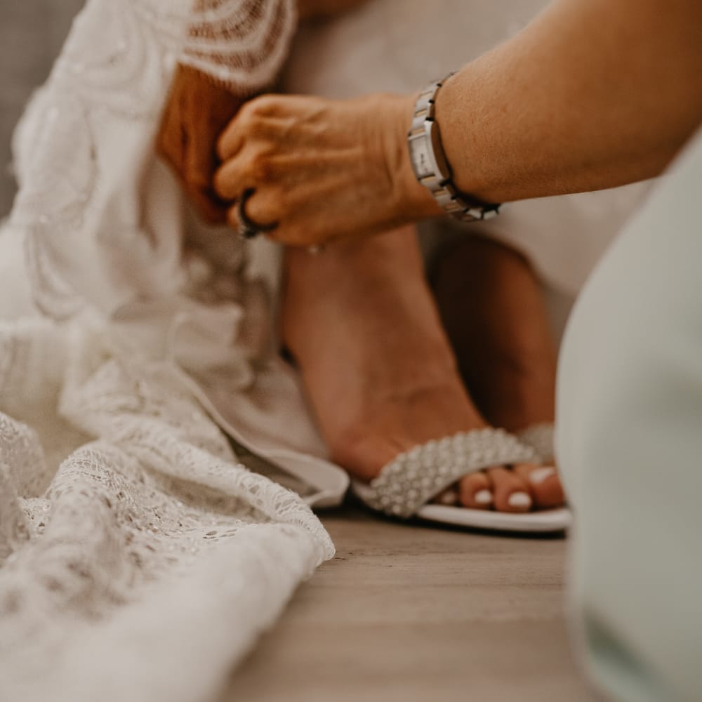 Bride has her wedding shoes done up by guest on her wedding day as she gets ready | Mark Bamforth Photography
