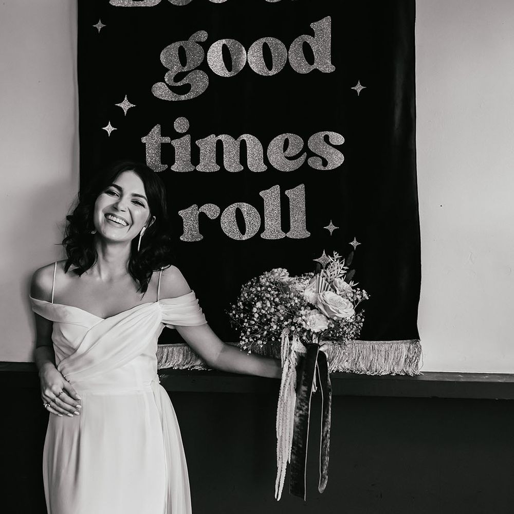 Bride in a cold shoulder wedding dress standing next to a let the good times roll wedding banner 