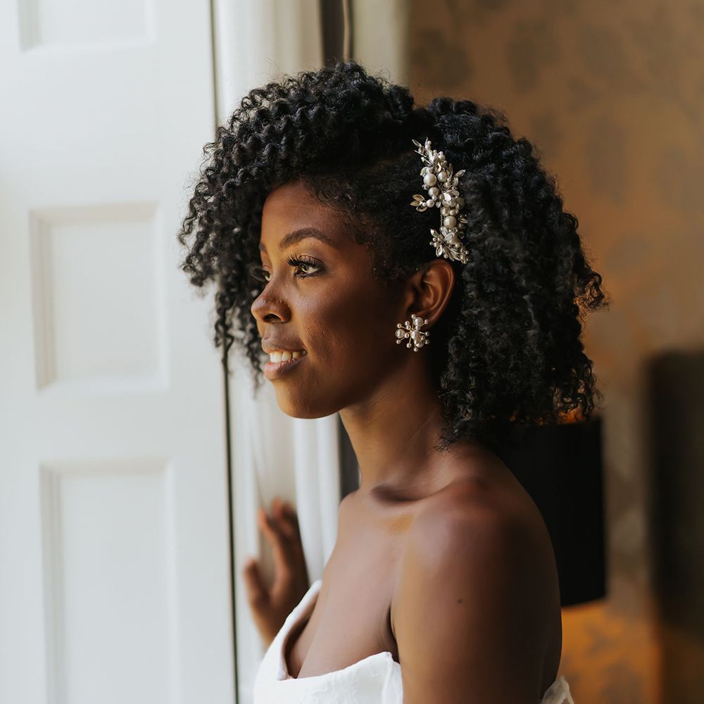 Black bride in a strapless wedding dress with naturally curly afro hair side swept and styled with a jewel hair slide 
