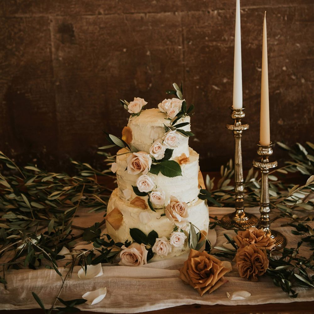 Three tier buttercream wedding cake decorated with blush roses on a cake table with candlesticks and taper candles 