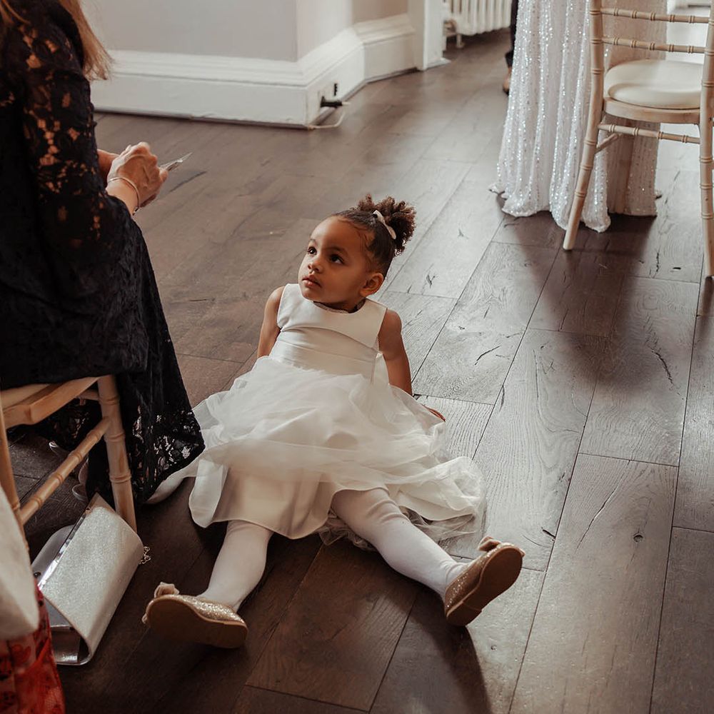 Flower girl wears white tea length dress with her hair in a top knot