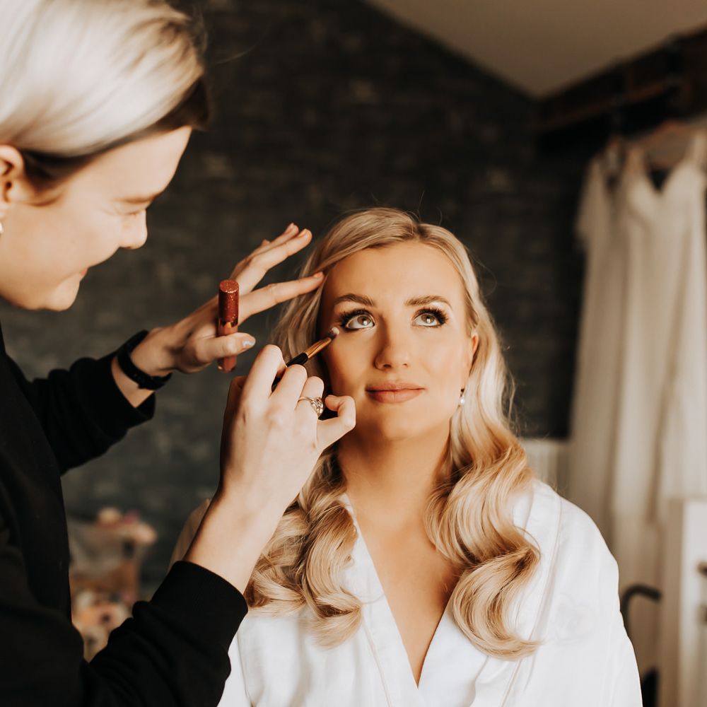 Bride with blonde curled hair has her makeup done before wedding