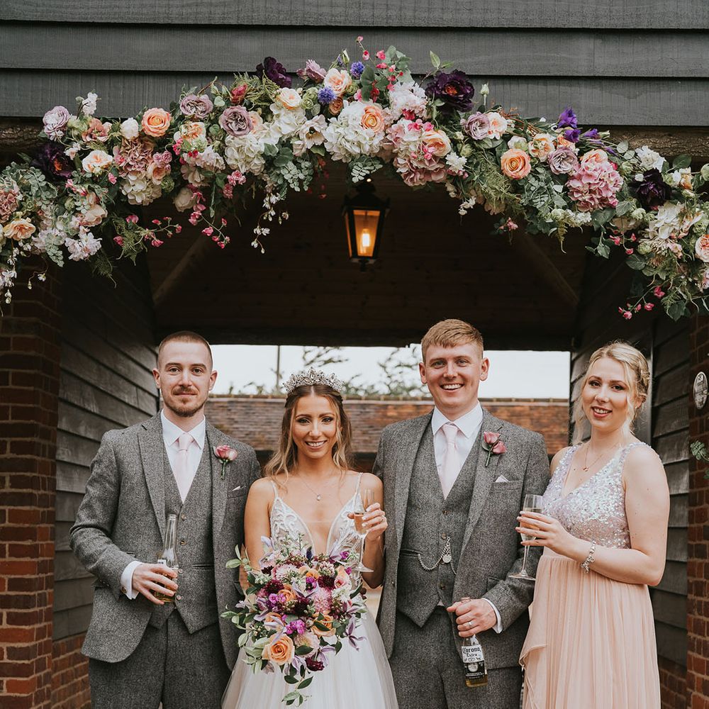 Bride and groom smile with bridesmaid and groomsman under arch of flowers of bright colours