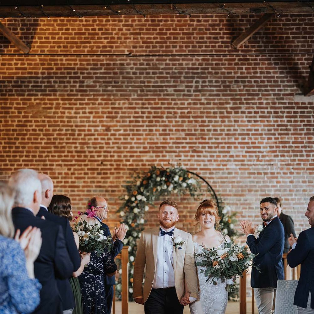 Bride and groom walk back down the aisle as a married couple with bride in lace Maggie Sottero dress 