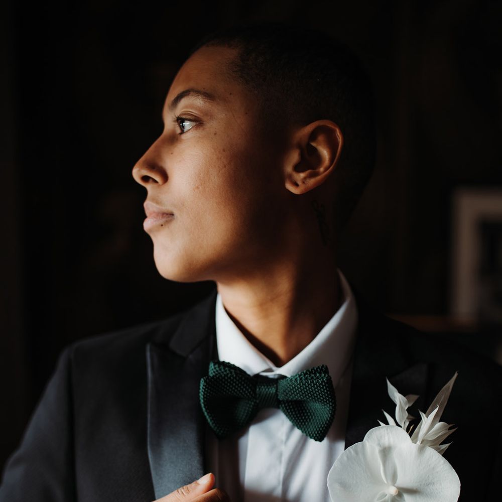 He/him in a black tuxedo and green bow tie with white orchid buttonhole flower 