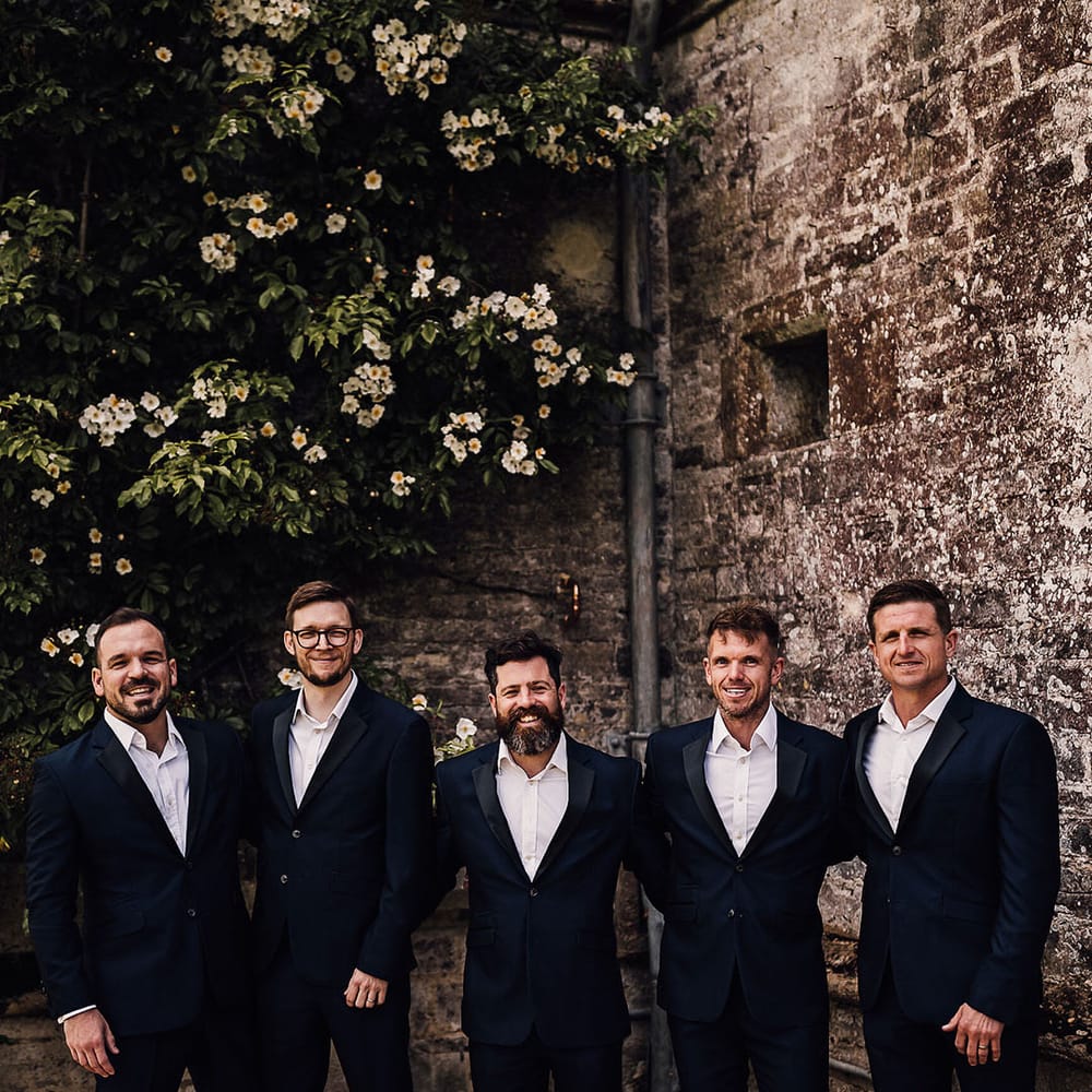 Groom and groomsmen in matching blue suits with black satin lapels for outdoor wedding at Athelhampton House 