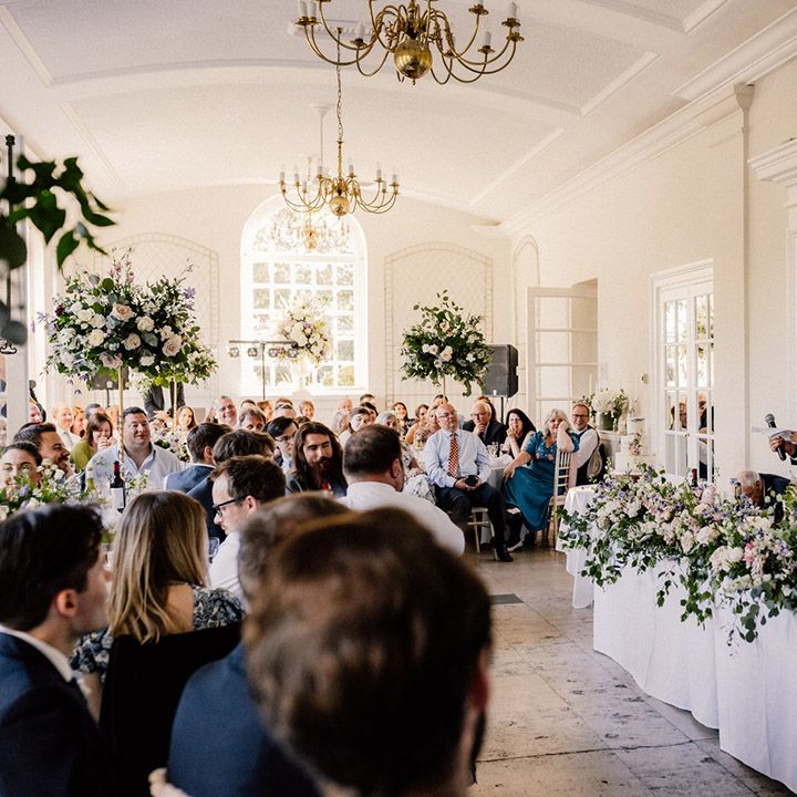 Father of the bride stands as he reads out his speech for traditional wedding with top table decorated with colourful spring flowers 