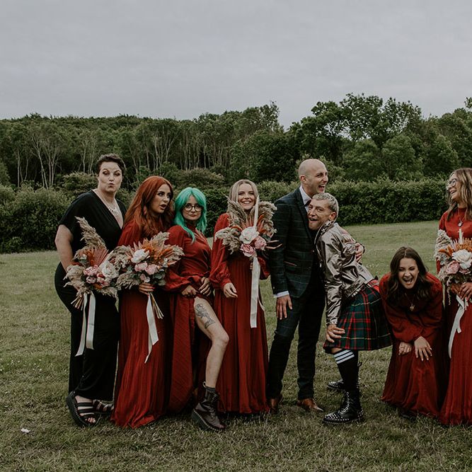 Grooms stand beside their bridesmaids who wear long sleeve red dresses complete with homemade floral bouquets 
