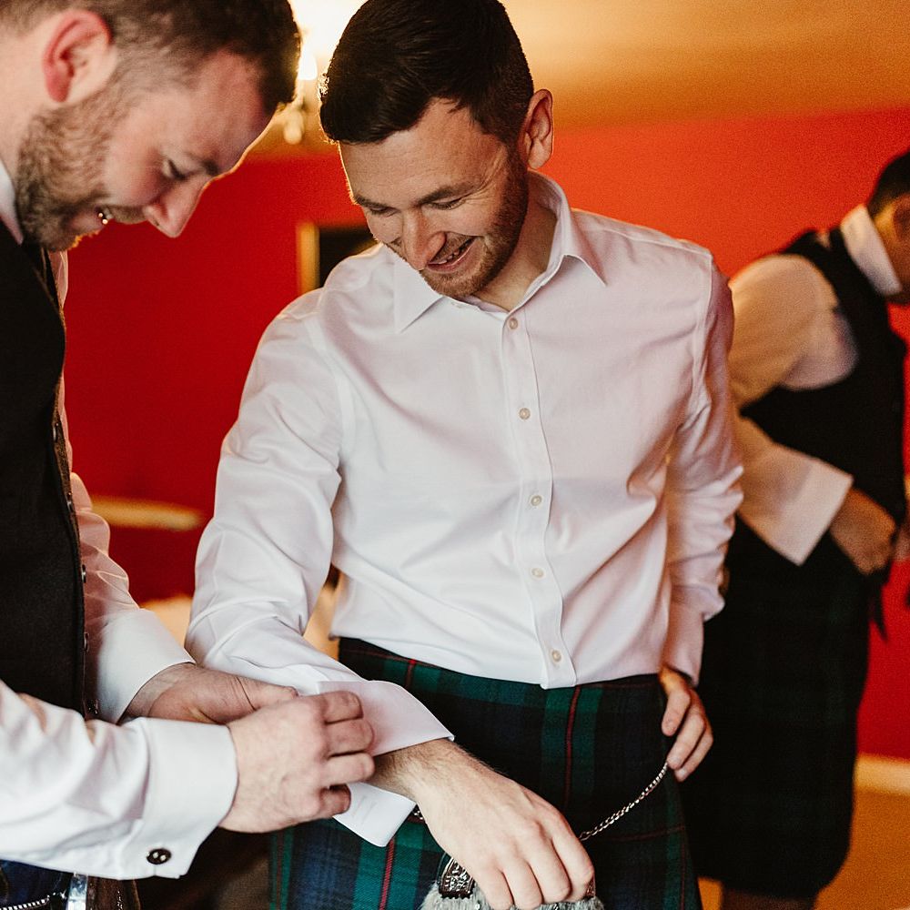 Groomsmen helps groom put on cufflinks on the morning of his wedding day 