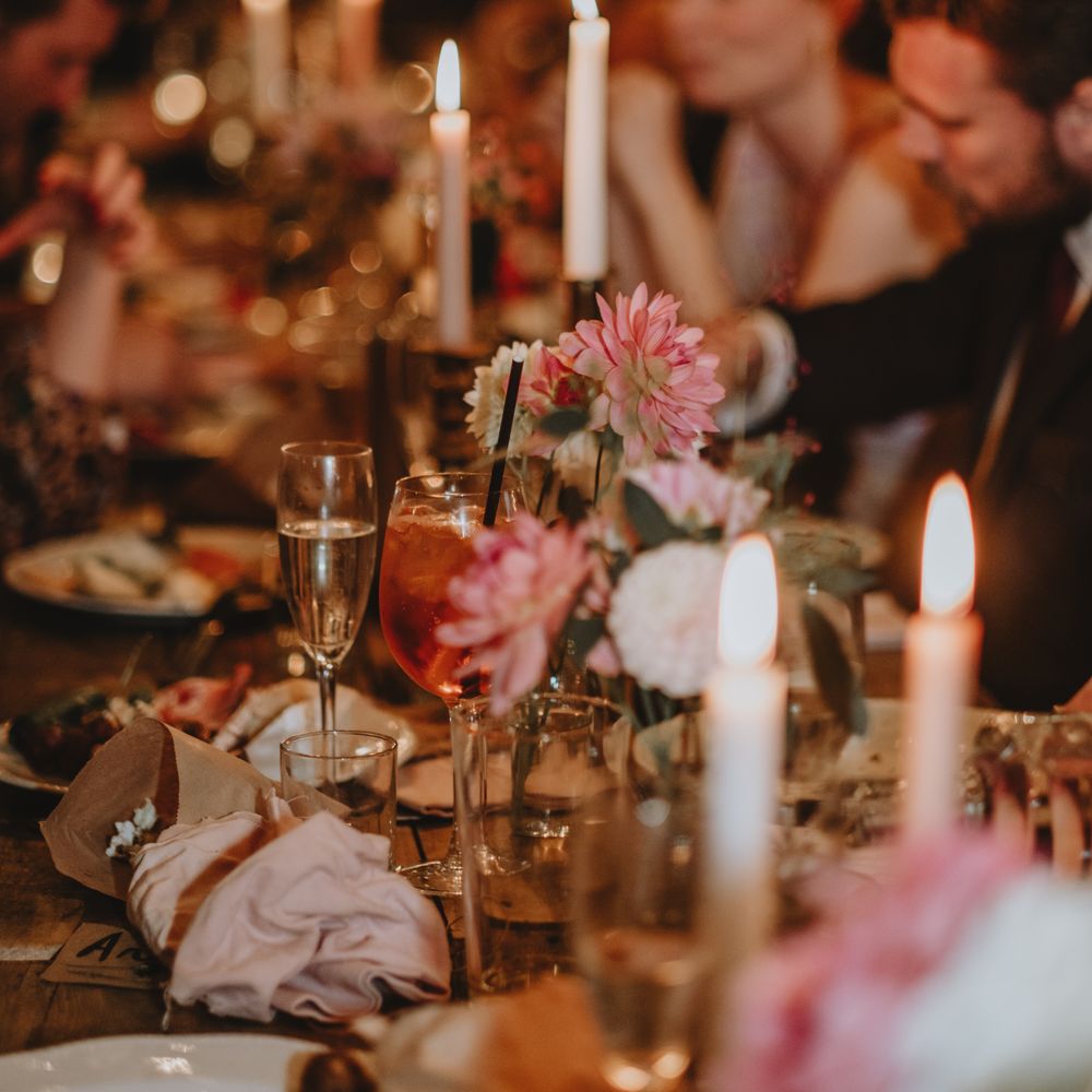 Small floral arrangements line wooden banquet tables alongside brown paper bags filled with popcorn 