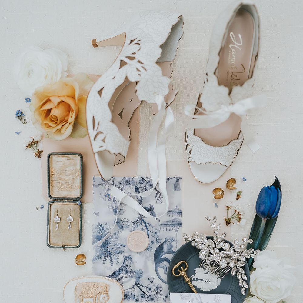 Diamond earrings and hair accessories with whit intricate wedding shoes, blue and orange flowers with stationery envelope