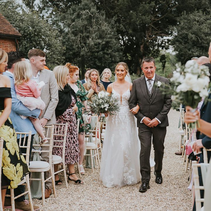 Bride is walked down the aisle by father in dark suit for the outdoor wedding ceremony at Stanlake Park wedding venue 