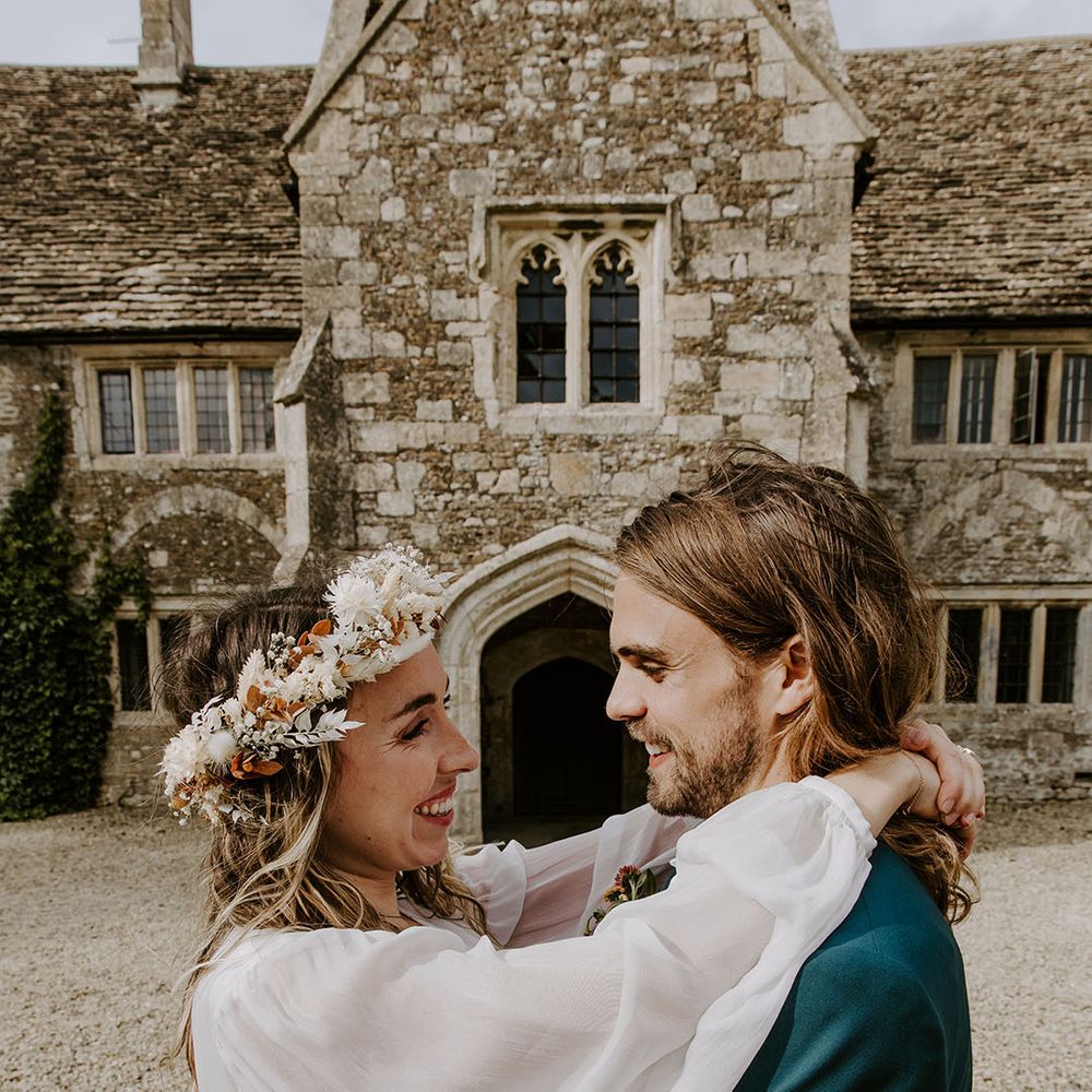 Bride wears boho styled floral crown and bell sleeved wedding dress whilst embracing her groom outdoors