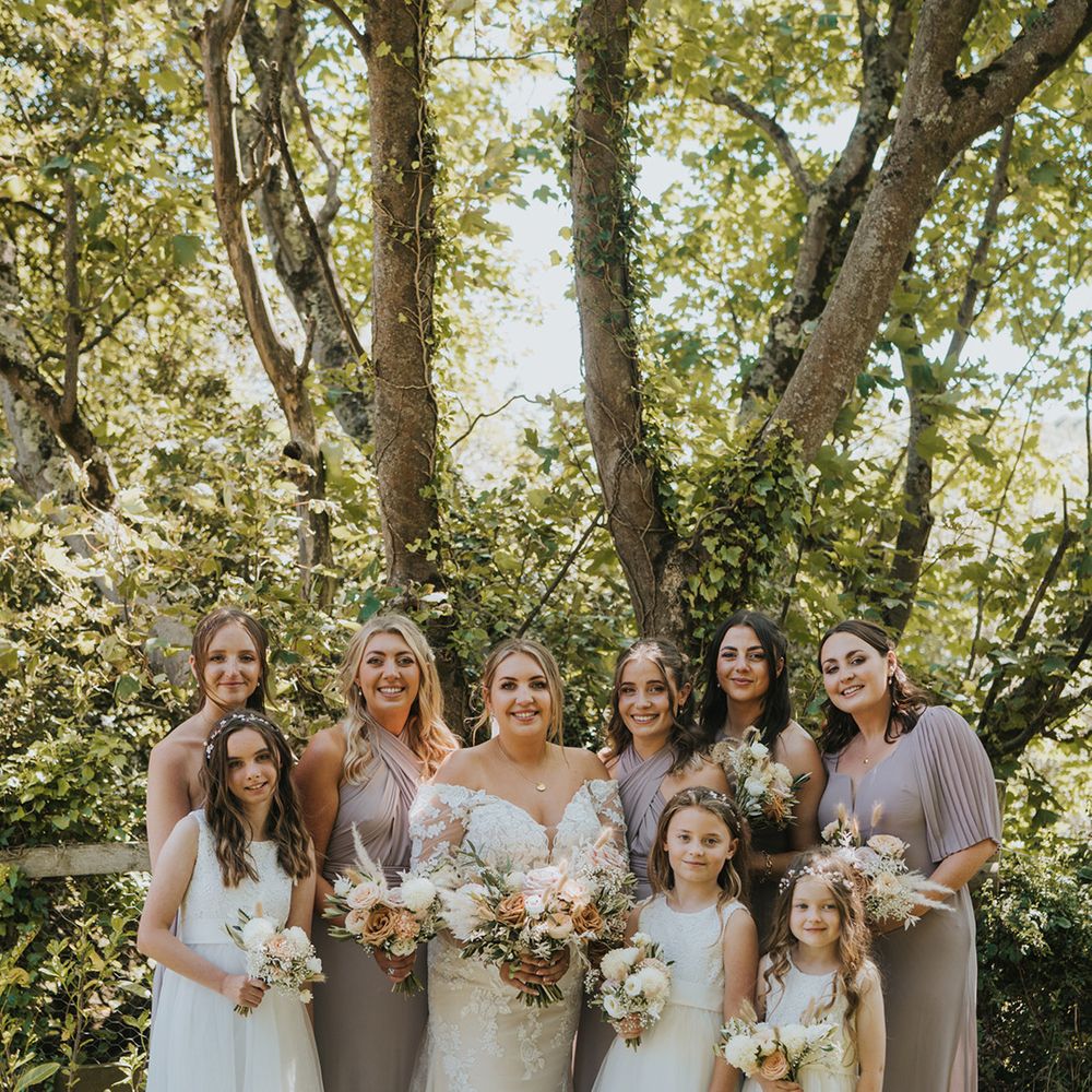 Bride stands with her bridesmaids in pink bridesmaid dresses and flower girls in matching princess styled dresses