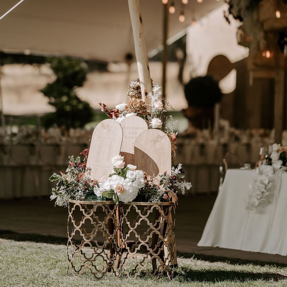 Small wooden arch seating chart with a neutral flower arrangement for marquee wedding 