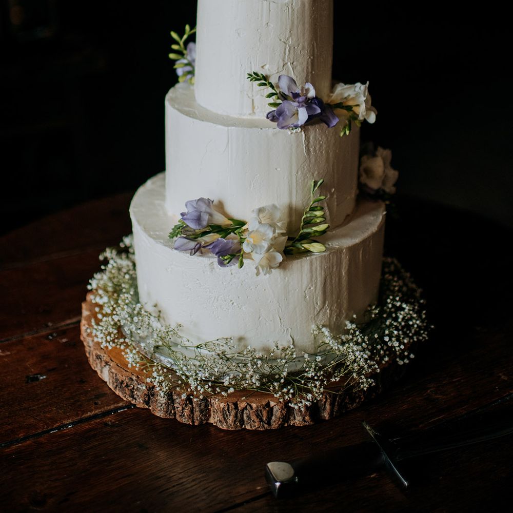 Three tier white frosted wedding cake complete with colourful floral decor on wooden block