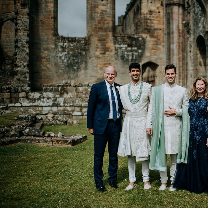 Grooms in matching white and sage green sherwani's stand outdoors with their family