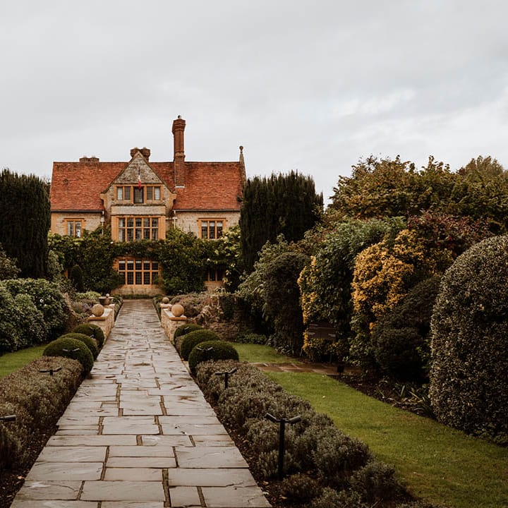 The exterior and gardens of Le Manoir Aux Quat Saisons with paving stone path leading to the venue 