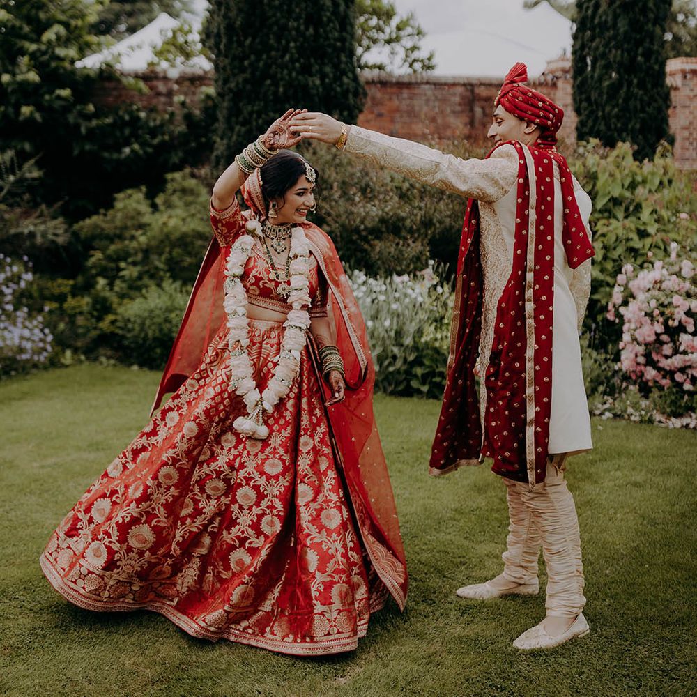 Groom in red and white sherwani spins his bride who wears red and gold lehenga 