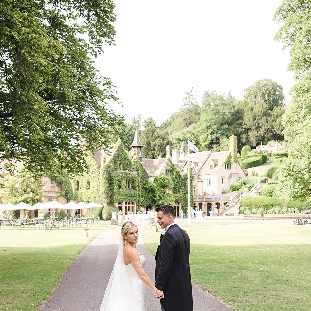 Bride in princess mermaid wedding dress with long cathedral length veil walking with the groom in a morning suit 