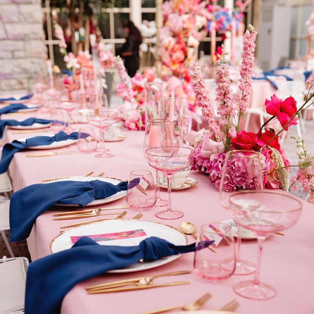 White plate with gold edges and gold cutlery with dark blue napkin and pink tablecloths and flowers 