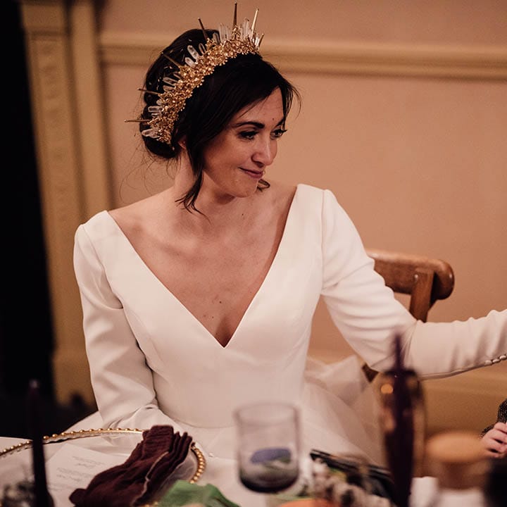 Bride in traditional wedding dress with long sleeves wearing gold bride crown sitting next to her son in brown suit 