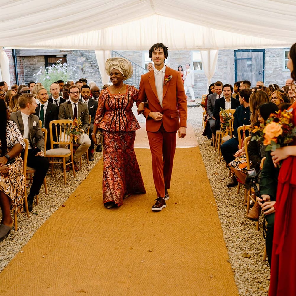 Wedding guests in orange and yellow wedding theme clothes walking down the aisle on orange wedding carpet at Broadfield Court