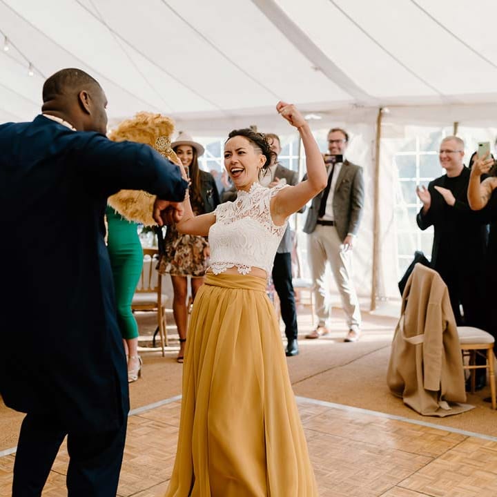 Groom in navy wedding suit dancing with bride in white mesh lace bridal crop top and yellow wedding skirt at Broadfield Court