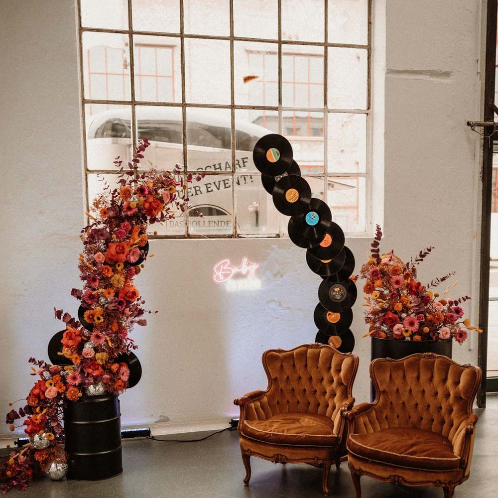 Vinyl wedding arch next to vibrant pink red and orange wedding floral arch and two crushed velvet burnt orange armchairs at German wedding