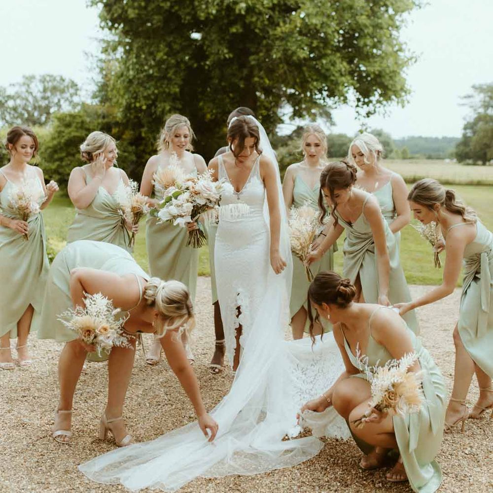 Bridesmaids in light green satin front twist bridesmaid dresses helping bride in v neck lace wedding dress with front slit and church length veil 