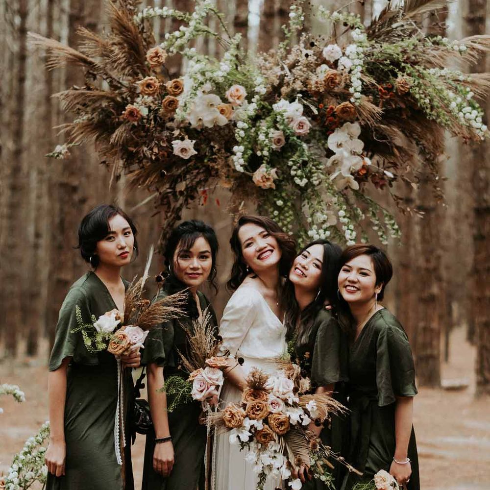 Bridesmaids standing with bride wearing forest green short sleeve front slit bridesmaid dresses in the forest 
