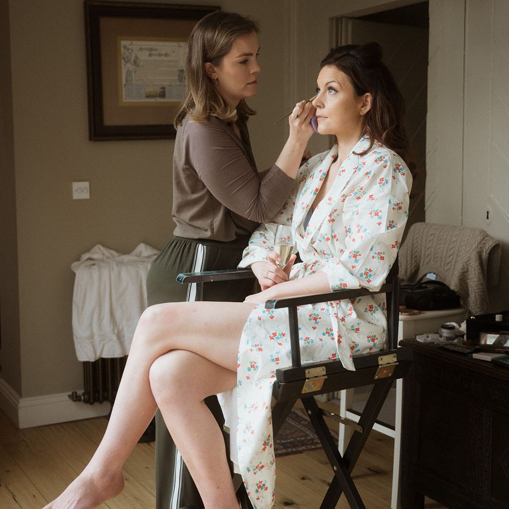 Bride in floral robe sits to get her wedding makeup done for the wedding 