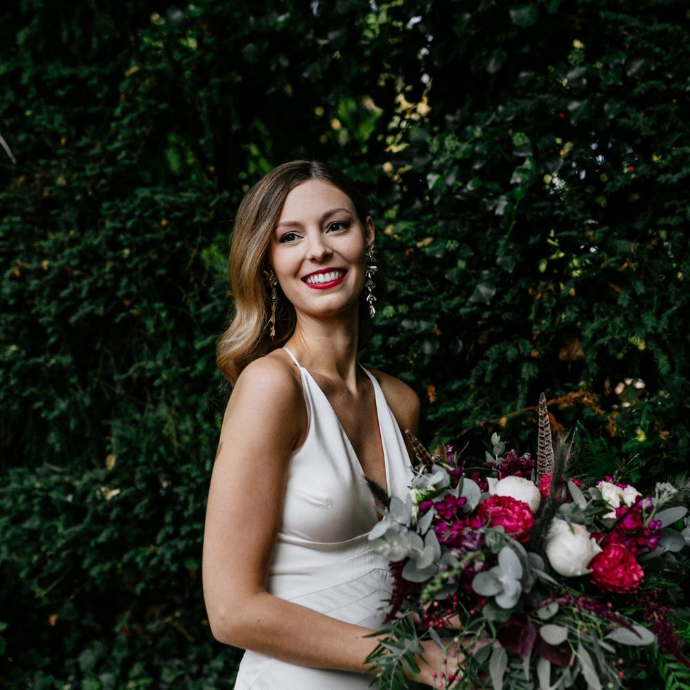 Stylish bride in ASOS wedding dress holding a red and white bouquet