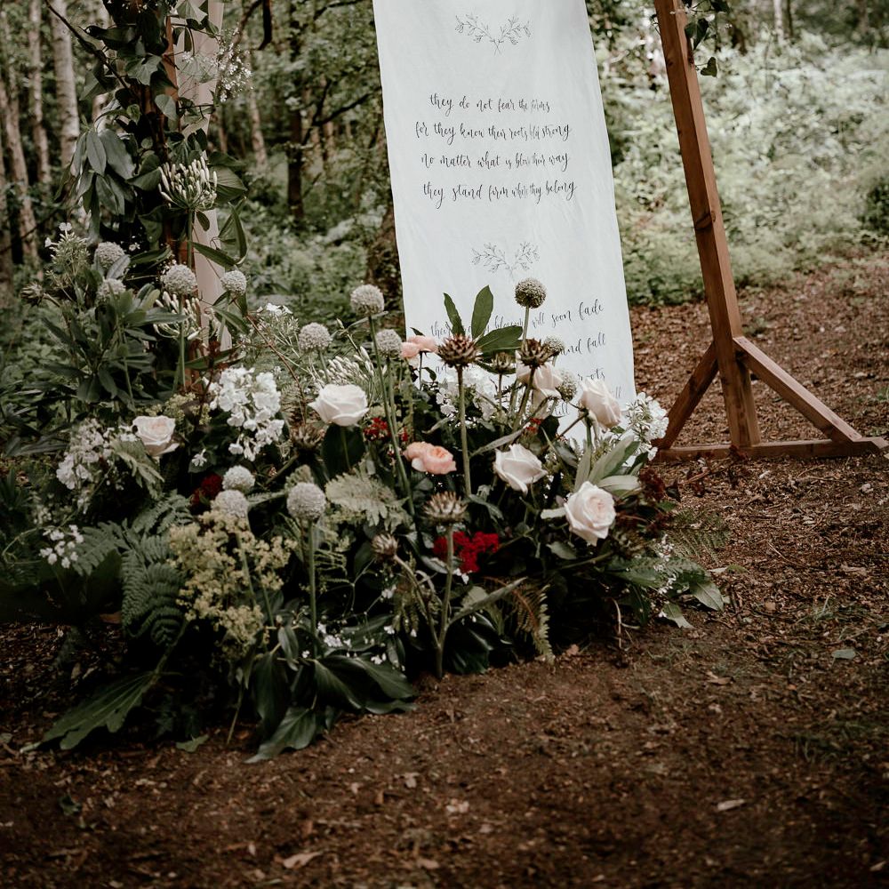 Wooden frame in the woods with fabric sign and locally sourced flowers