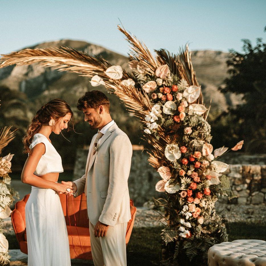 Outdoor hand fasting ceremony for boho bride and groom at their floral moon gate and wicker rug altar 