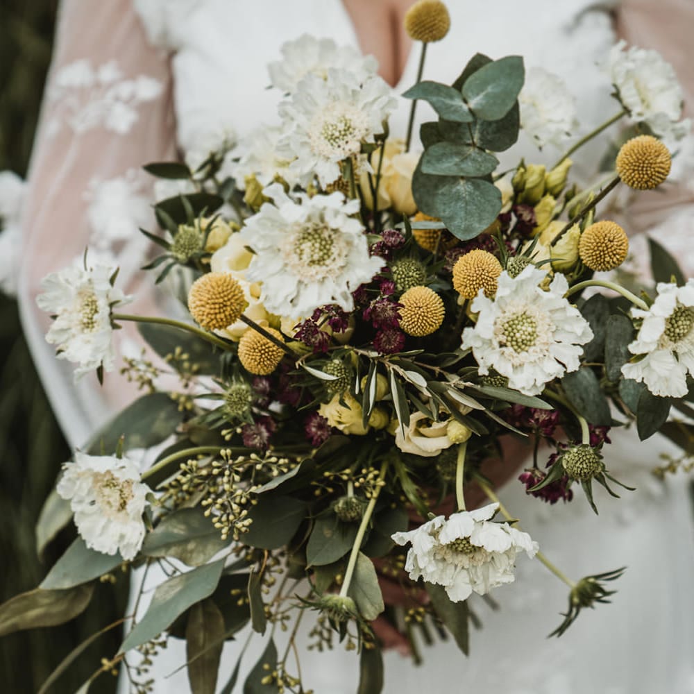 Unstructured wedding bouquet with white flowers, foliage and yellow Billy Buttons 