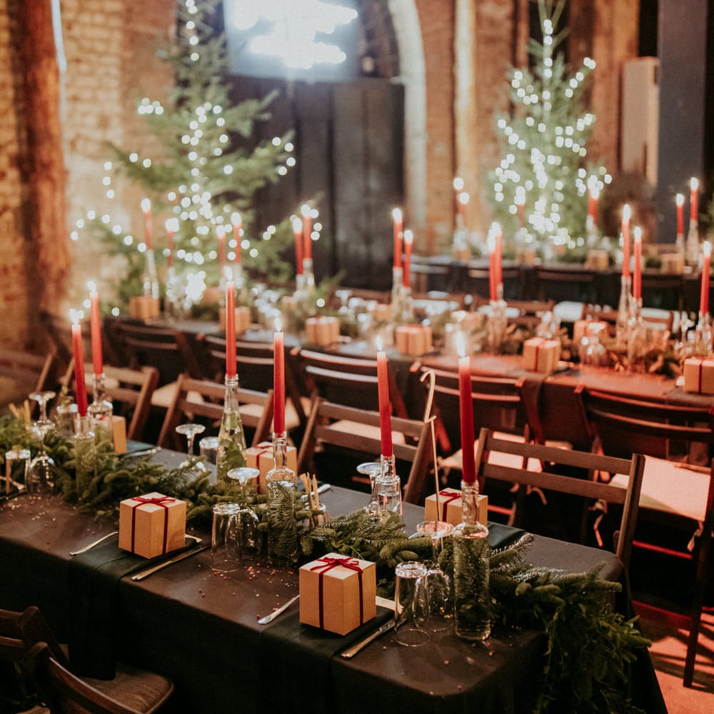 Banquet tables with tapered candles, bottles filled with water and eucalyptus and brown wedding favour boxes