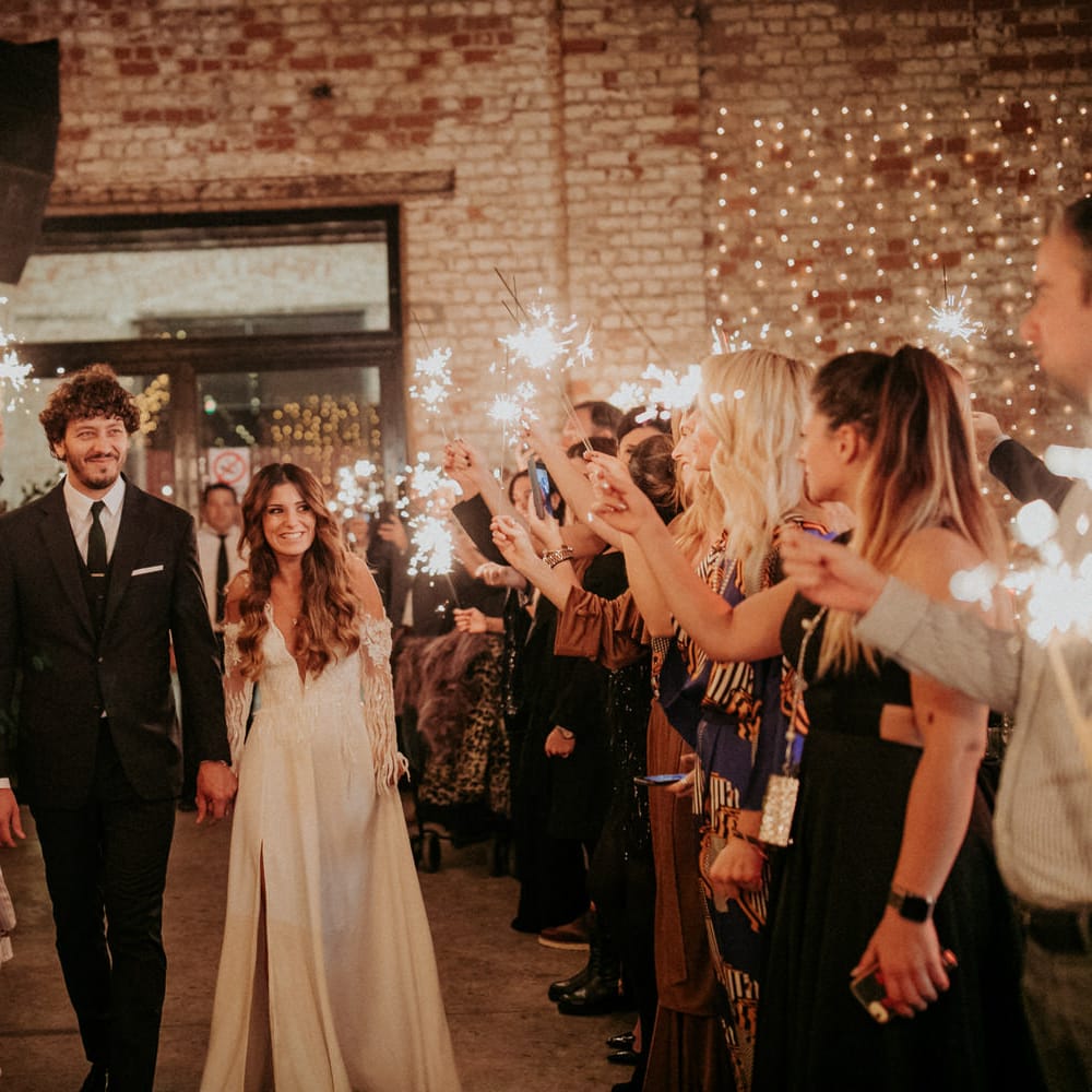 The bride and groom leaving their Block 33 wedding reception in the evening as their guests hold up sparklers