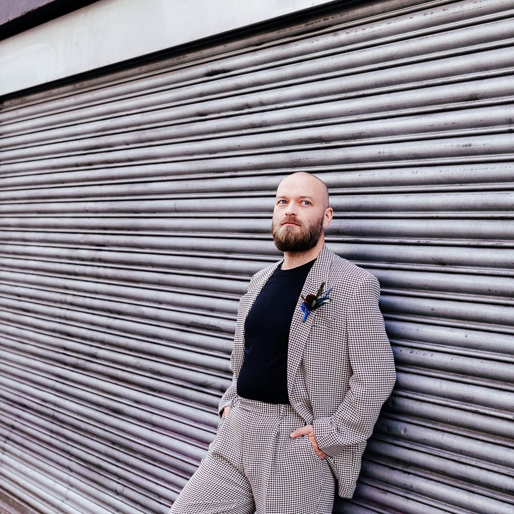 Groom in a check wedding suit, black t-shirt and feather buttonhole 