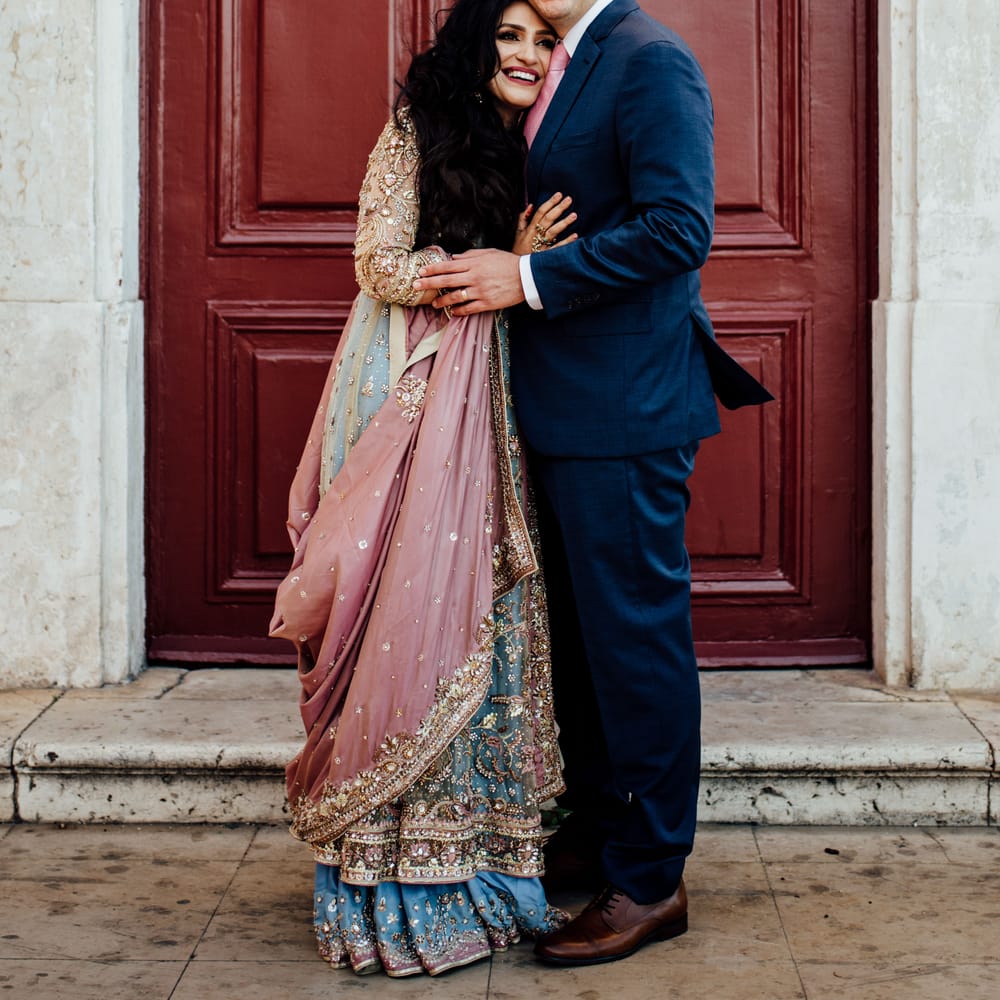 Bride rests her head on grooms chest as she wears brightly coloured saree 